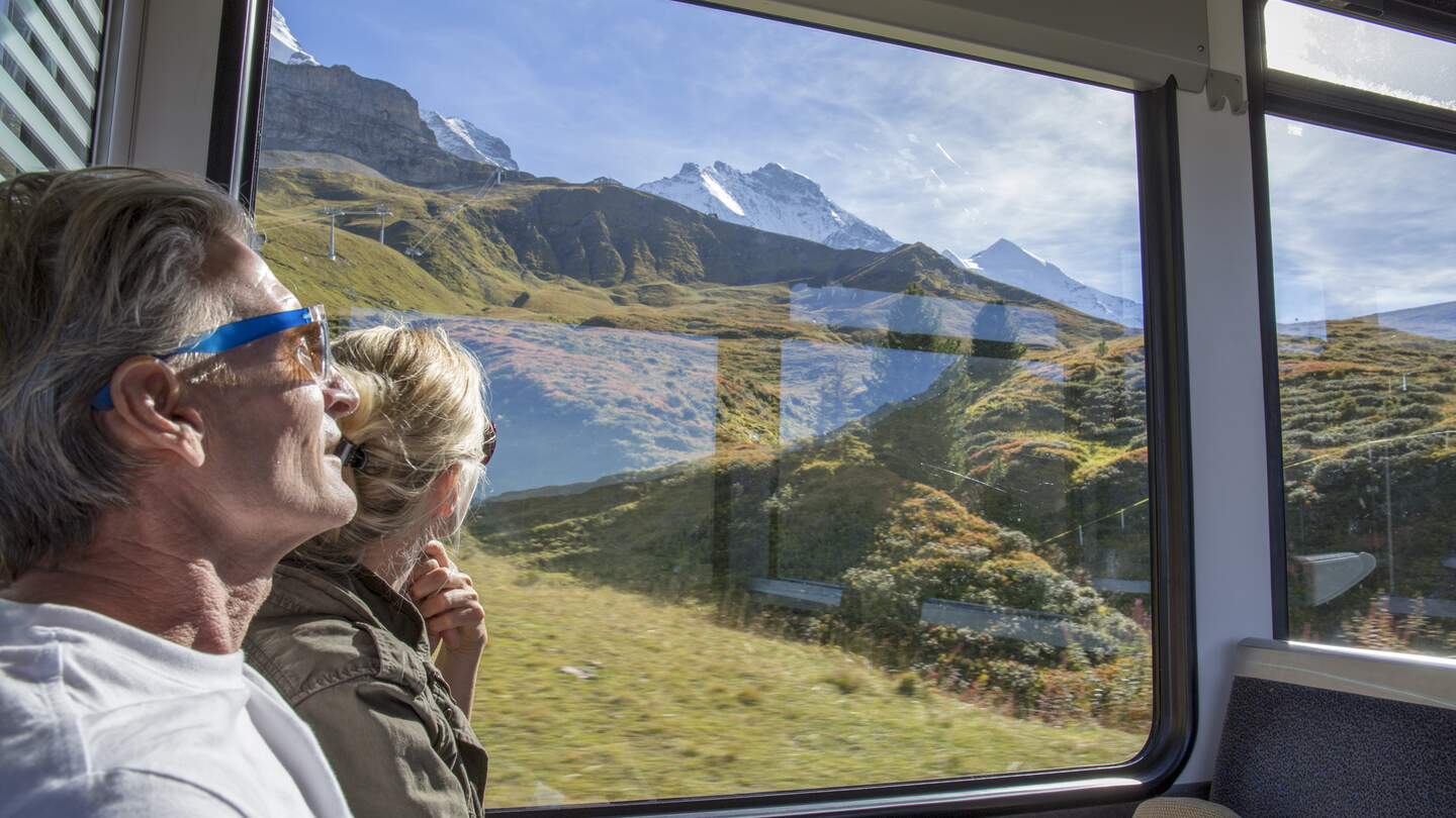 Bestager-Paar genießt den Blick aus einem Zugfenster, auf das sonnige Panorama der Schweizer Berge | © Gettyimages/AscentXmedia