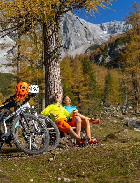 Sportliches reiferes Paar enstpannt sich nach Fahhrradfarht mit Elektro-Mountainbikes auf einer Bank in der alpinen Berglandschaft | © Gettyimage/amriphoto