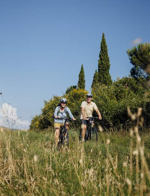 Seniorenpaar fährt mit Mountainbikes bei gutem Wetter über ein Feld bei blauem Himmel | © Gettyimage/SolStock