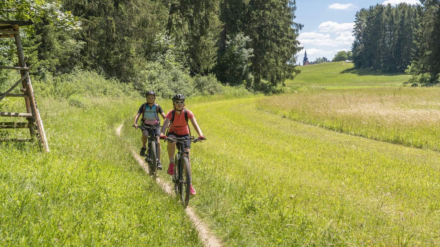 Zwei Frauen fahren mit Mountainbikes in der Fränkischen Schweiz über ein strahlend grünes Feld, Bayern | © GettyImages.com/Uwe Moser
