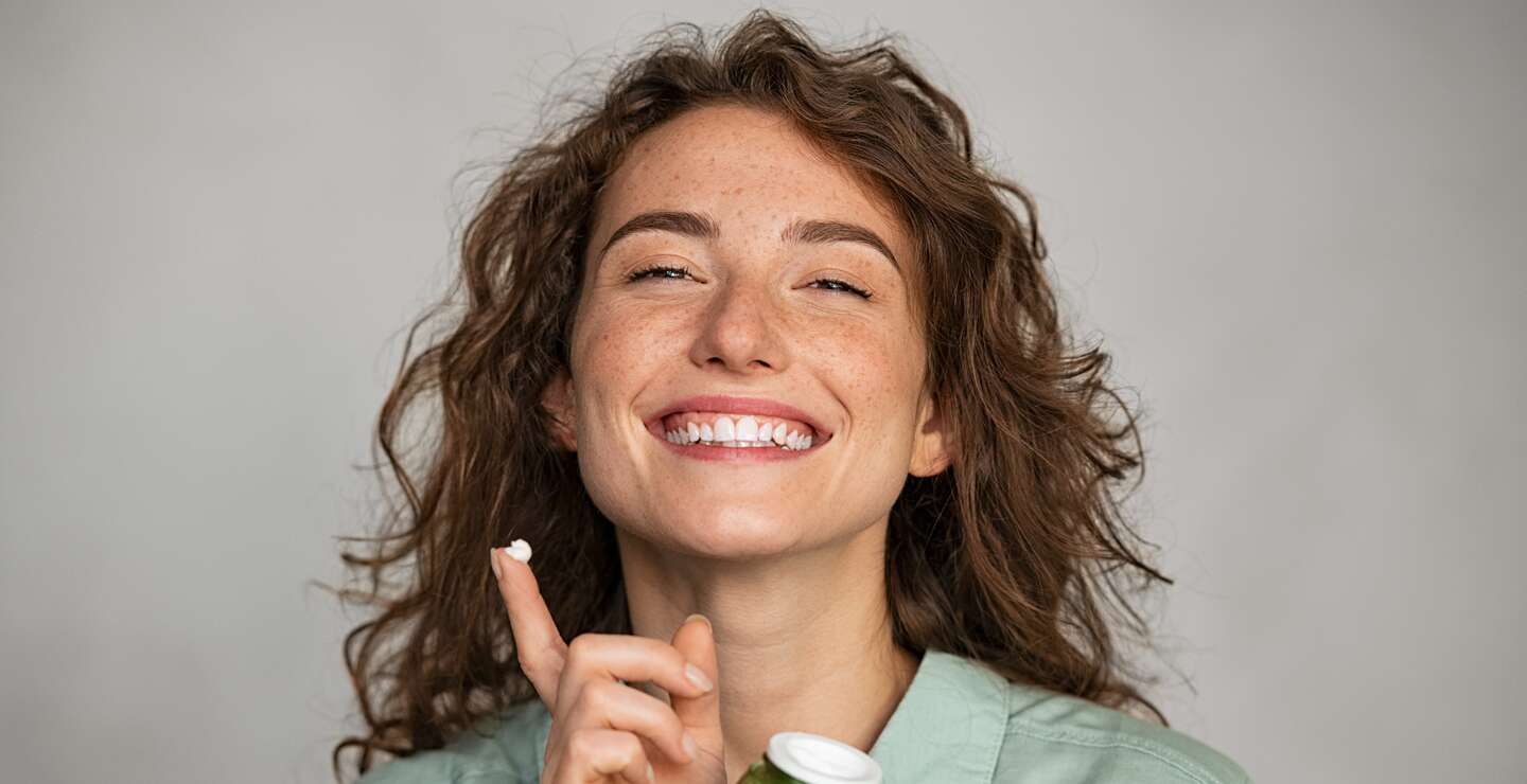 Schöne lächelnde Frau Anwendung Gesichtscreme aus grünem Glas | © Gettyimages.com/Ridofranz