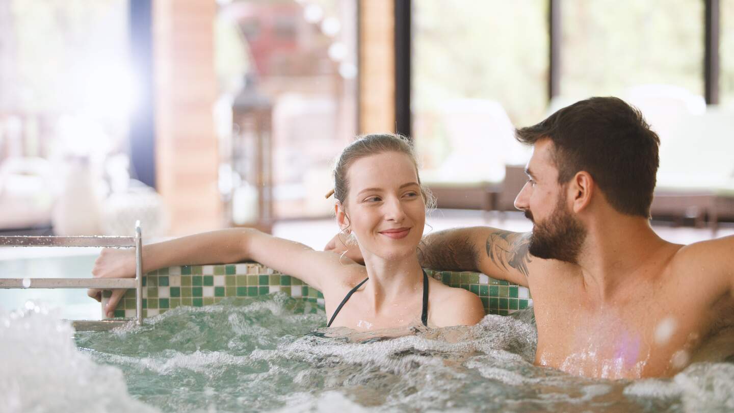Glückliches Paar sitzt in einem Whirlpool im Spa-Resort | © Gettyimages.com/fotostorm